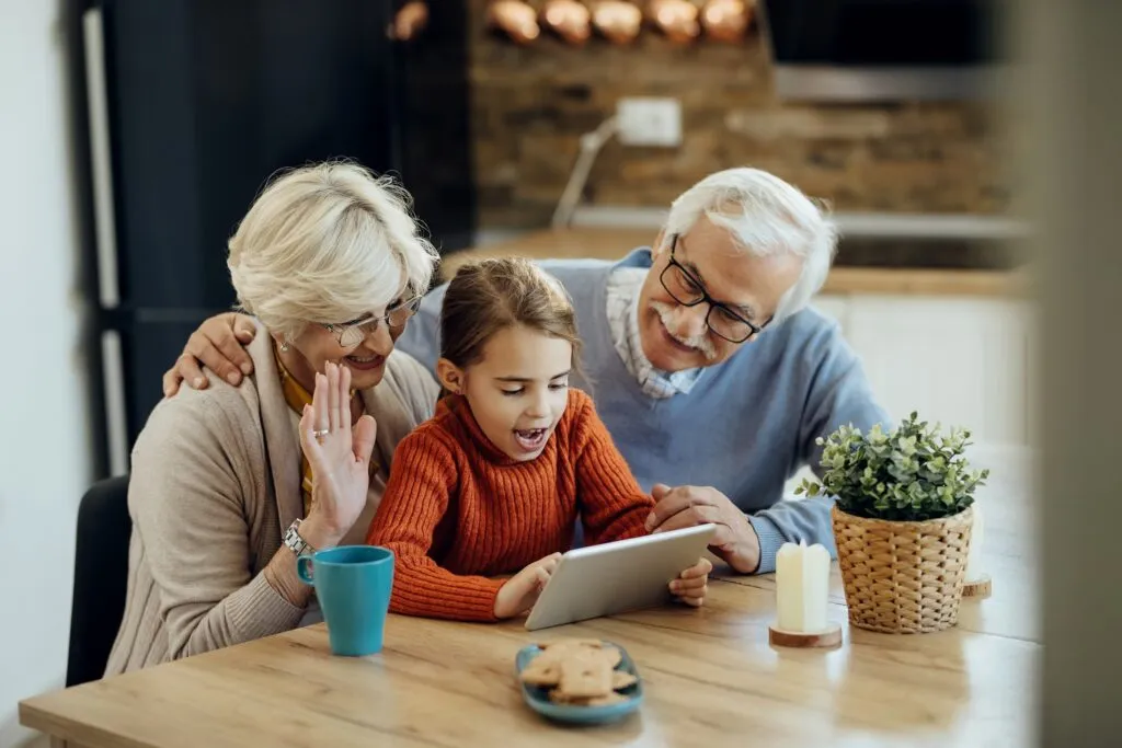 Grandparents and their granddaughter laughing together over a tablet